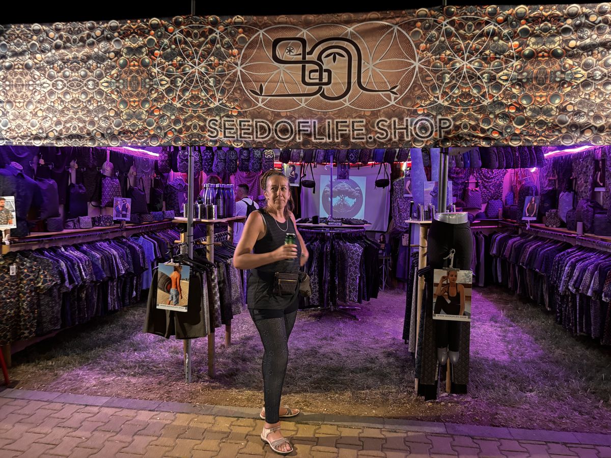SOL Seed of Life festival booth at night at Ozora, psychedelic clothing on display